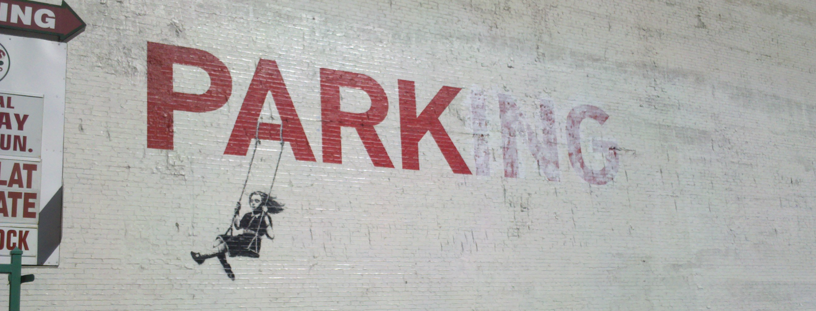 Banksy modified a parking sign painted on a wall to say "park" and drew a girl on a swing hanging from the letter A.
