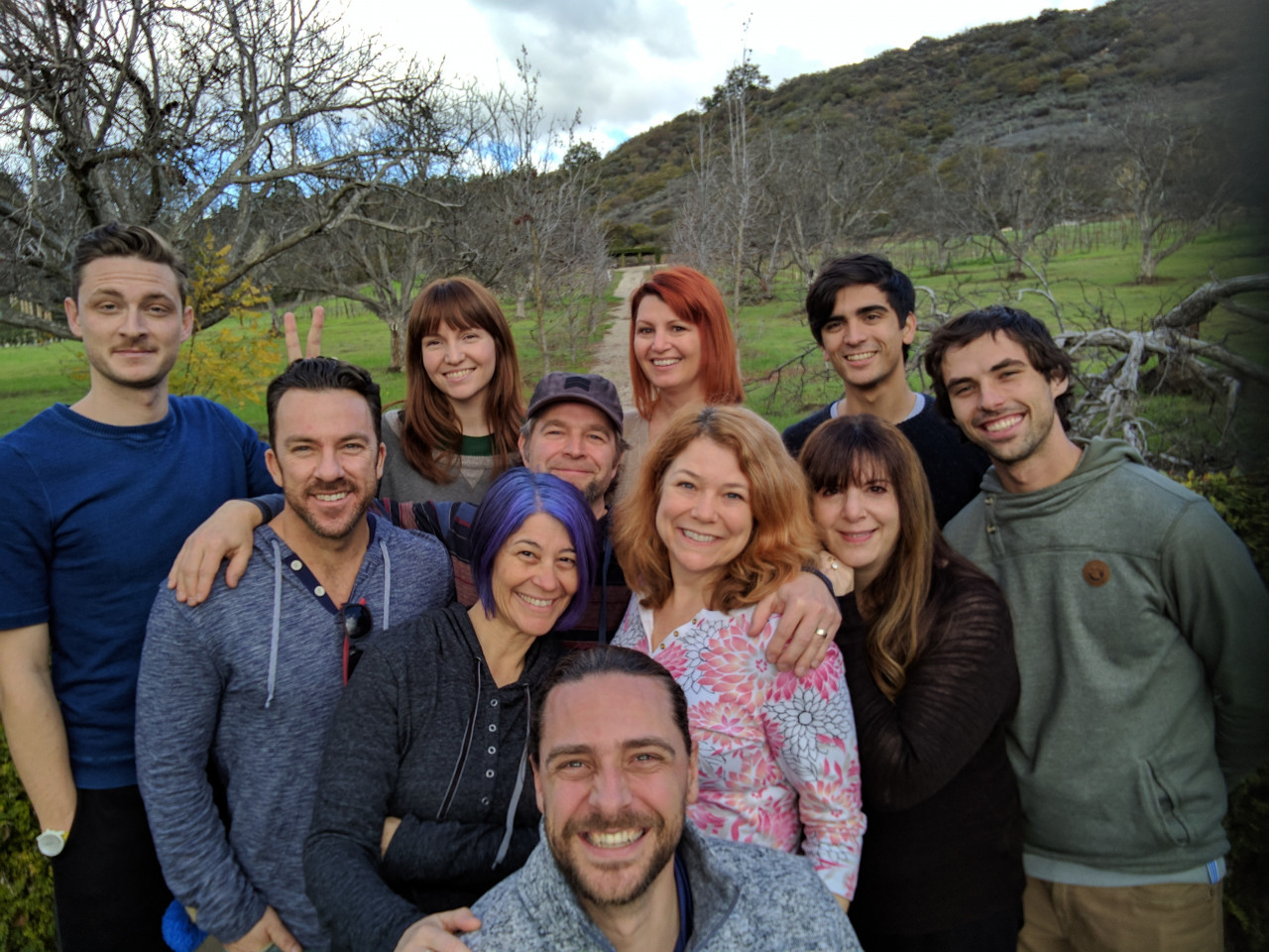 A group picture of smiling Primitive Spark people in Ojai, California in a lush wooded area.